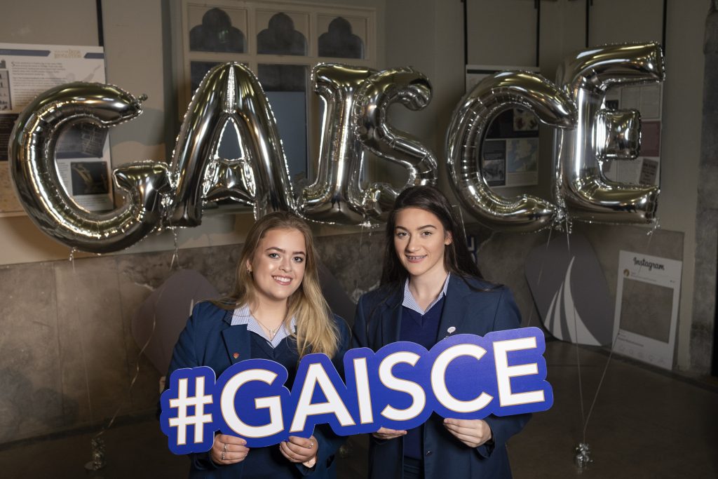 2 teenage girls holding a sign that says '#Gaisce'