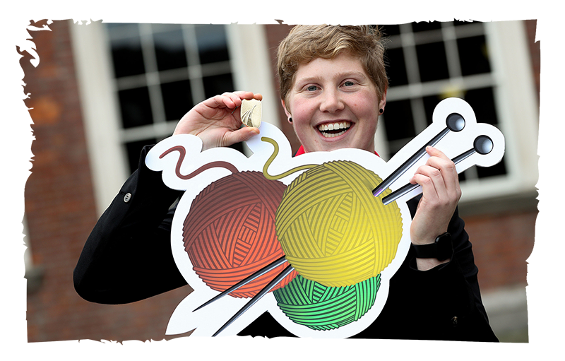 Olivia Porter Sketch Gold Awardee showing off their medal and holding an image of knitting needles and yarn.