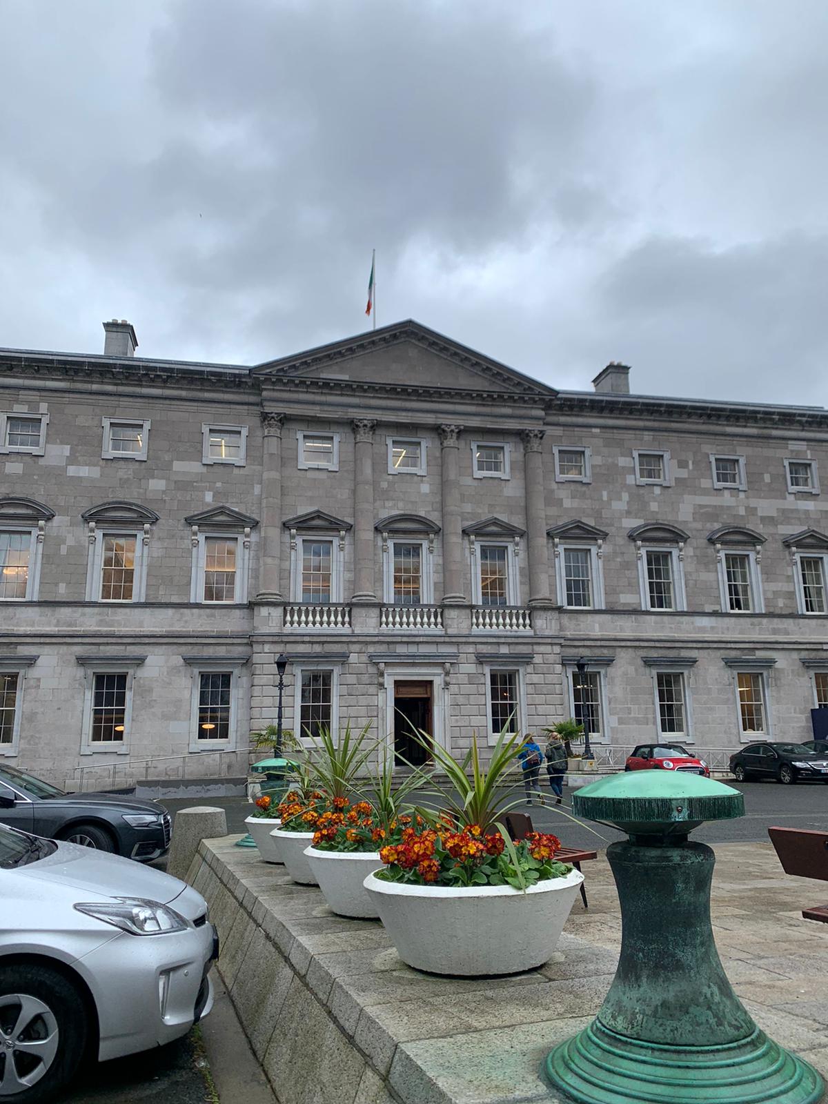 Outside of Leinster House. The building is classical looking and has round pots of flowers decorating the walkway to the door.