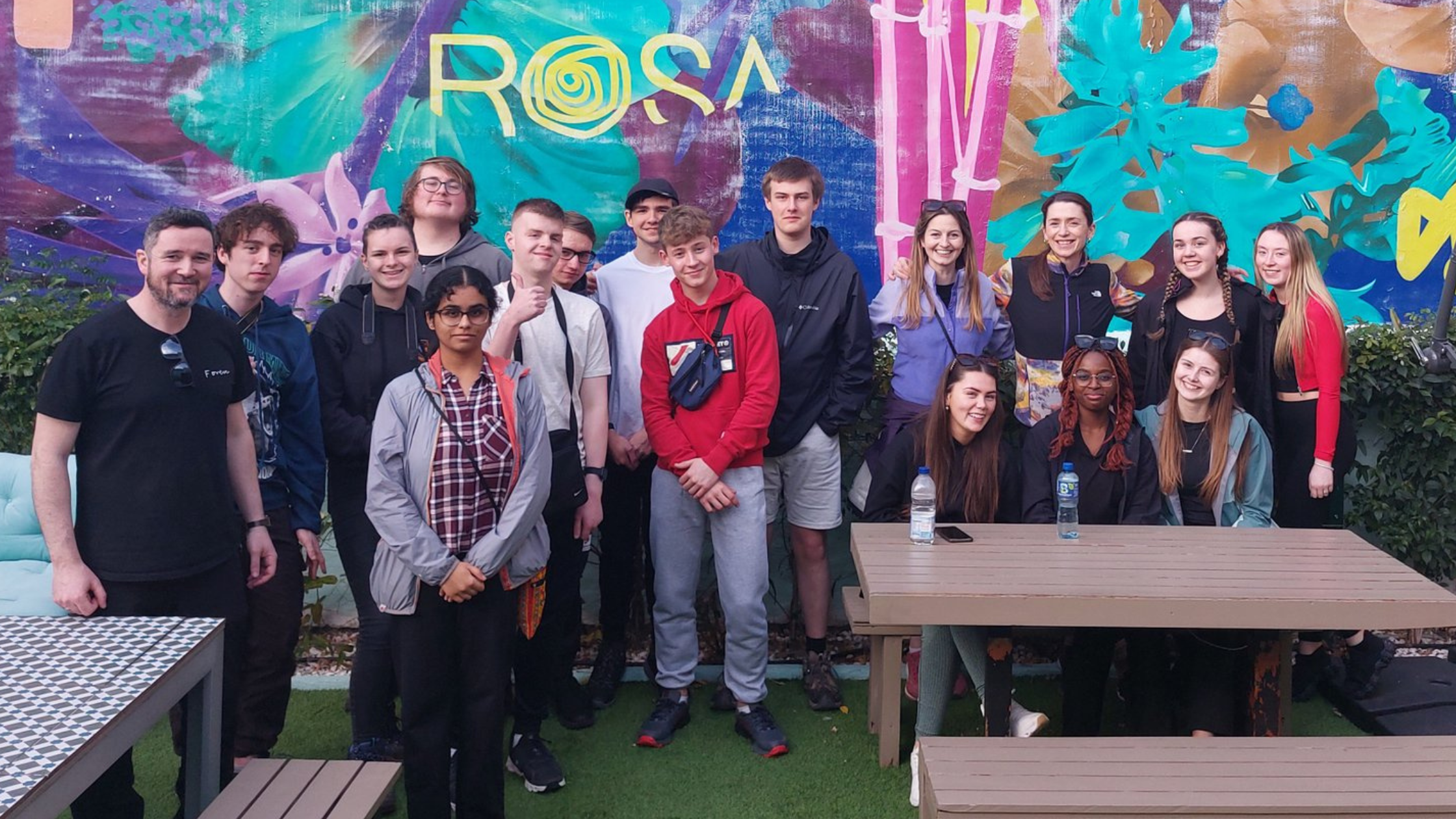 Group of students from Pobalscoil Neasáin posing in front of a vibrant wall with the text "Rosa" on it.